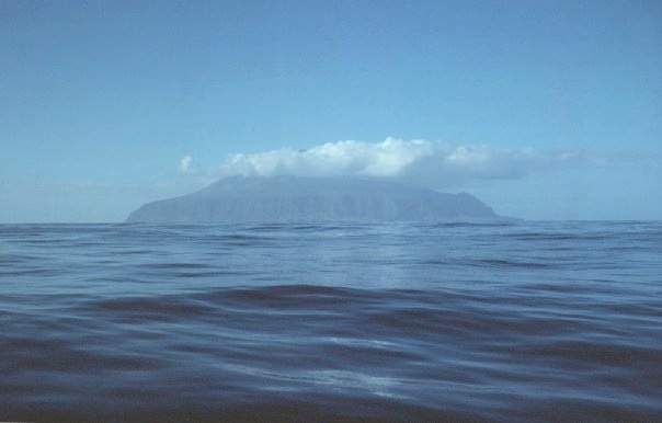 Tristan da Cunha visible from sea level, a dark volcanic cone with cloud across its summit.